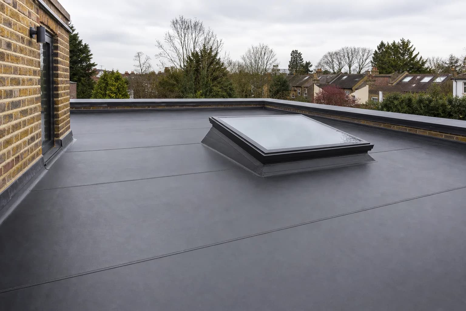 A modern flat roof freshly laid with dark grey EPDM rubber membrane, clean welded seams and lead flashing