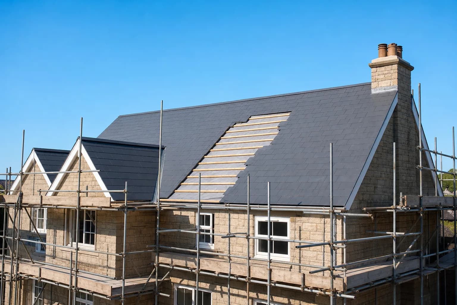 A house with scaffolding around a newly re-tiled pitched roof, fresh grey slate tiles over timber battens
